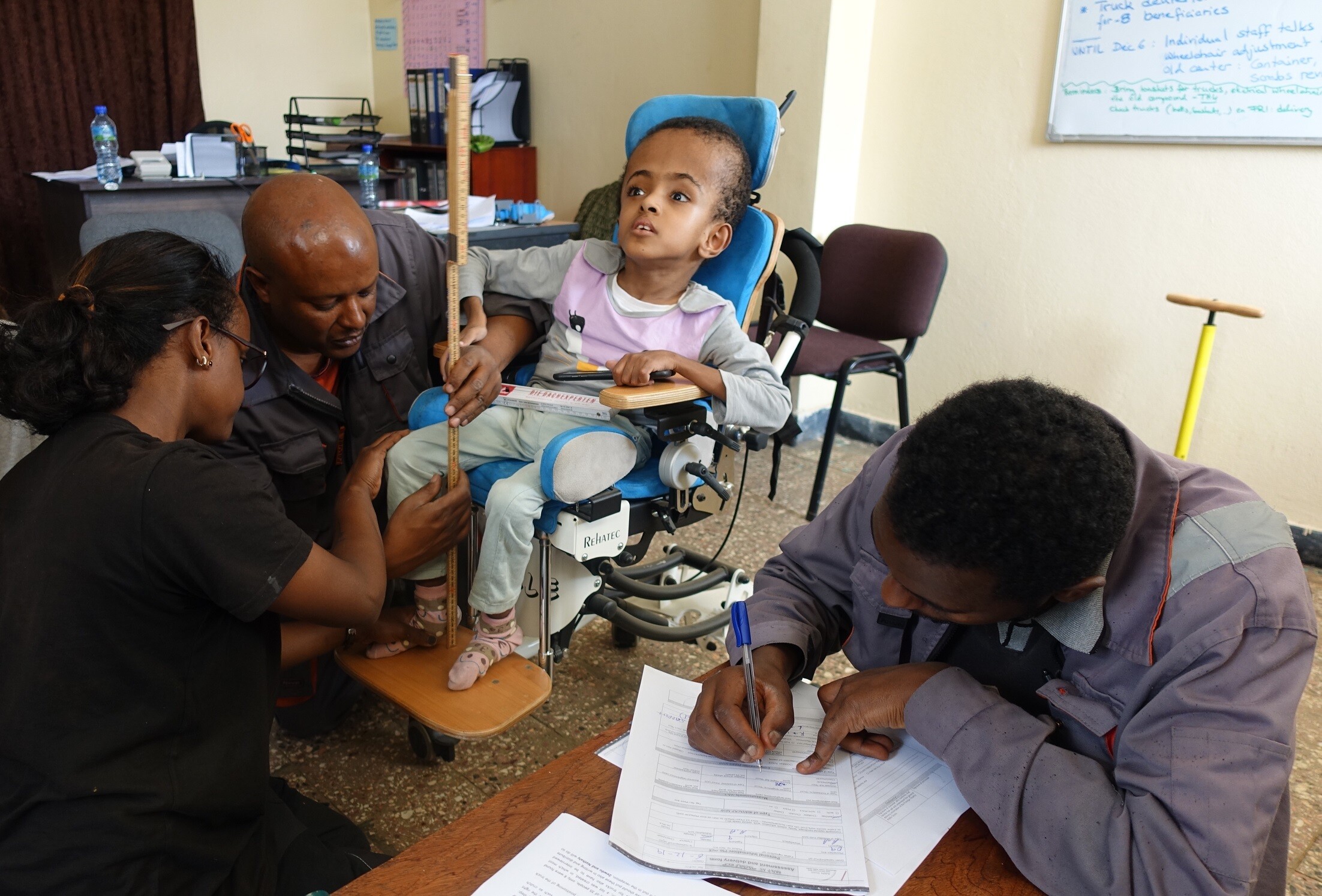 Drei Mitarbeitende von Addis Guzo messen bei einem Kind im Rollstuhl die Sitzhöhe aus.