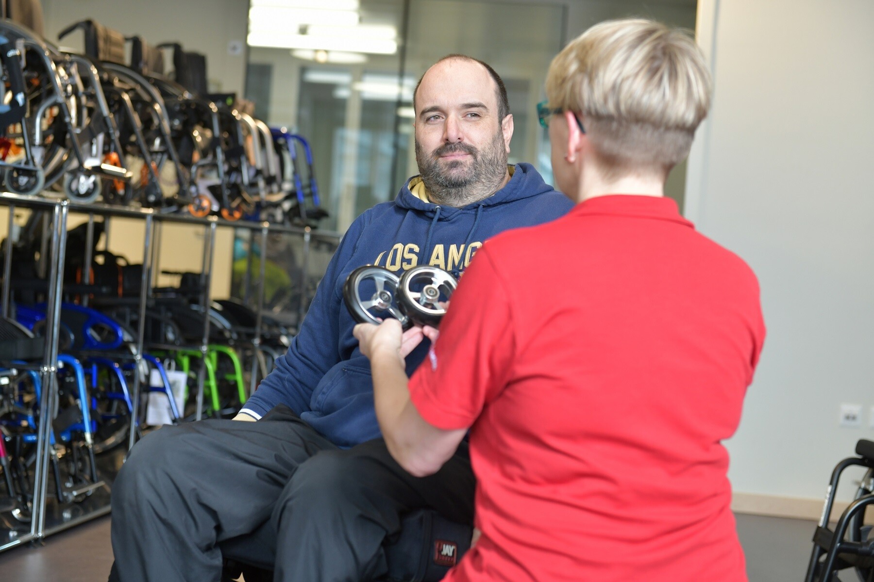 Une collaboratrice de Orthotec conseille un utilisateur de fauteuil roulant et lui montre deux roues avant.