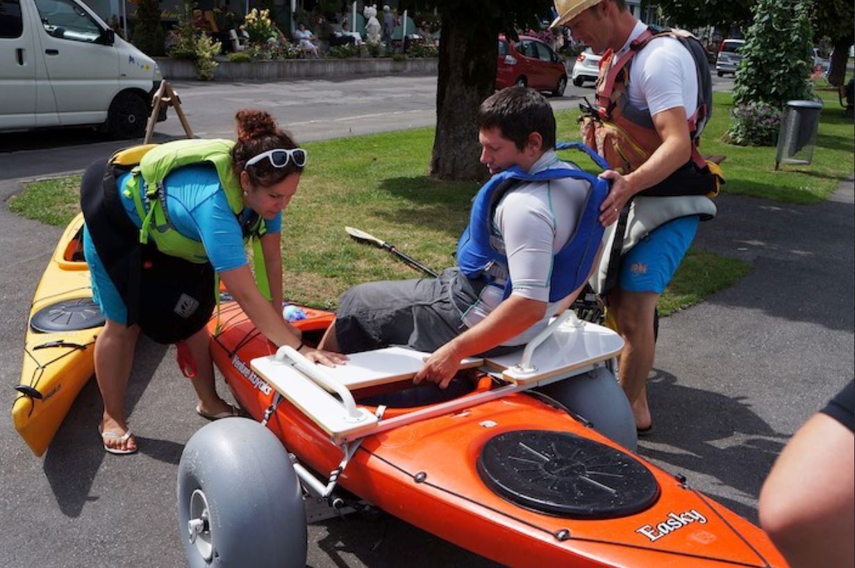 Una persona si trasferisce dalla carrozzina al kayak aiutandosi con un tavolo di trasferimento.
