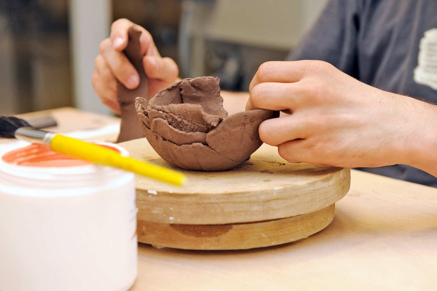 Due mani lavorano su una palla di argilla adagiata su una tavola di legno.